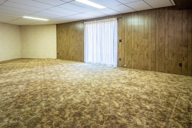 empty room featuring a drop ceiling, wood walls, and carpet