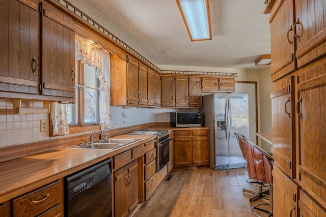 kitchen with a sink, wooden counters, appliances with stainless steel finishes, light wood-type flooring, and brown cabinetry