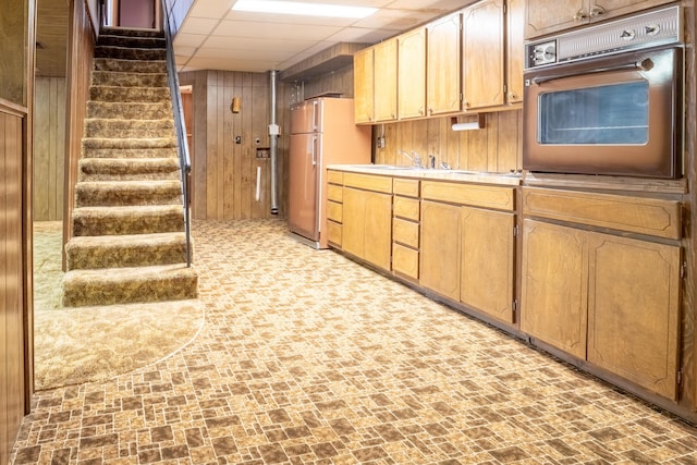 kitchen featuring a drop ceiling, brick floor, oven, wood walls, and freestanding refrigerator