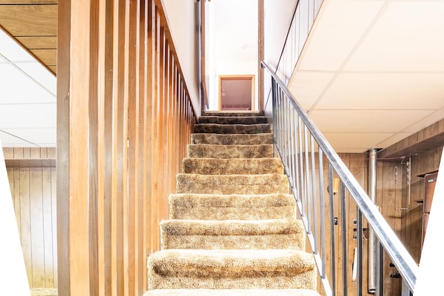 staircase with a paneled ceiling and wooden walls