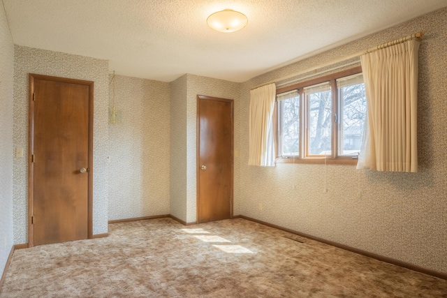 unfurnished bedroom featuring wallpapered walls, carpet, baseboards, and a textured ceiling