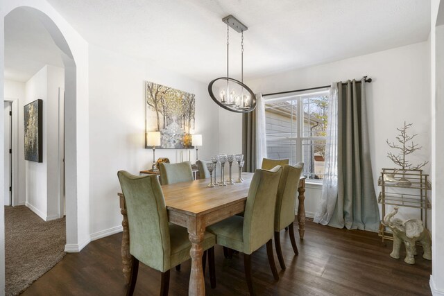 dining room with arched walkways, an inviting chandelier, baseboards, and dark wood-style flooring