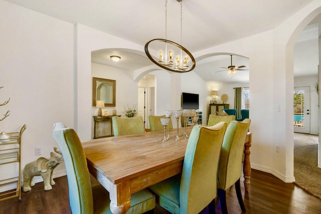 dining room featuring arched walkways, baseboards, lofted ceiling, and wood finished floors