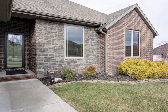 view of side of home with a shingled roof, stone siding, brick siding, and a yard