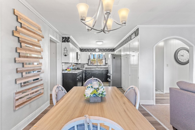 dining room with dark wood-style floors, arched walkways, a notable chandelier, ornamental molding, and baseboards