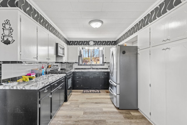 kitchen with appliances with stainless steel finishes, light wood-style floors, crown molding, and dark cabinets