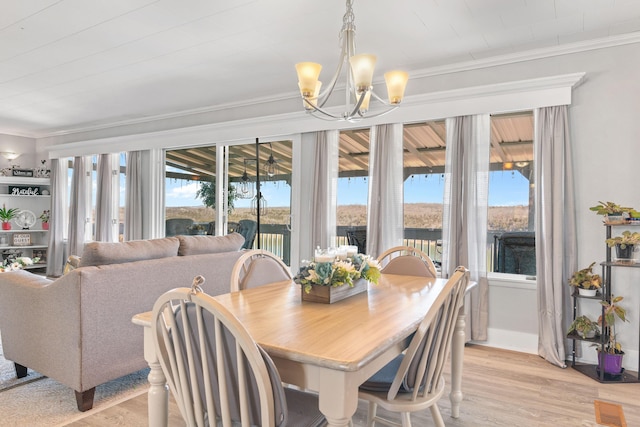 dining area with light wood-style floors, baseboards, ornamental molding, and a notable chandelier