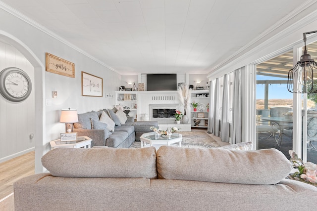 living area featuring a glass covered fireplace, wood finished floors, built in shelves, and crown molding