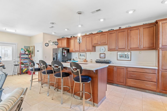 kitchen with a breakfast bar area, visible vents, brown cabinetry, and black fridge