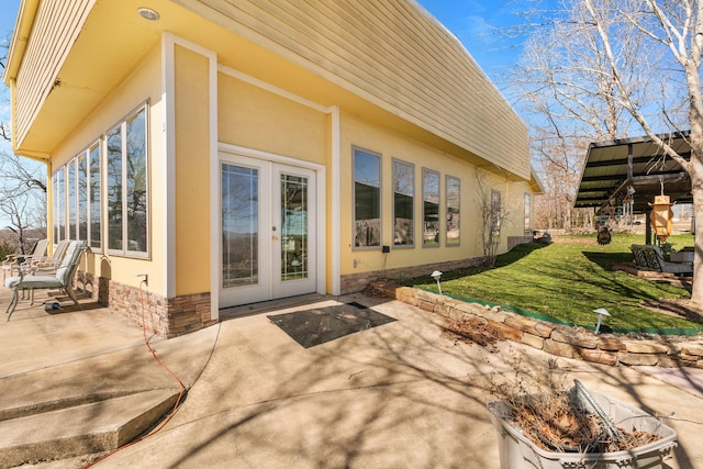 back of property with stone siding, a lawn, a patio area, and stucco siding