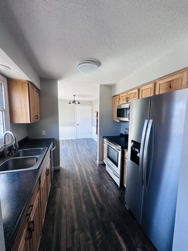 kitchen featuring dark wood-style floors, dark countertops, appliances with stainless steel finishes, a sink, and a textured ceiling