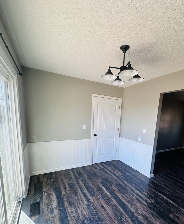 empty room with a textured ceiling, visible vents, dark wood-type flooring, and wainscoting