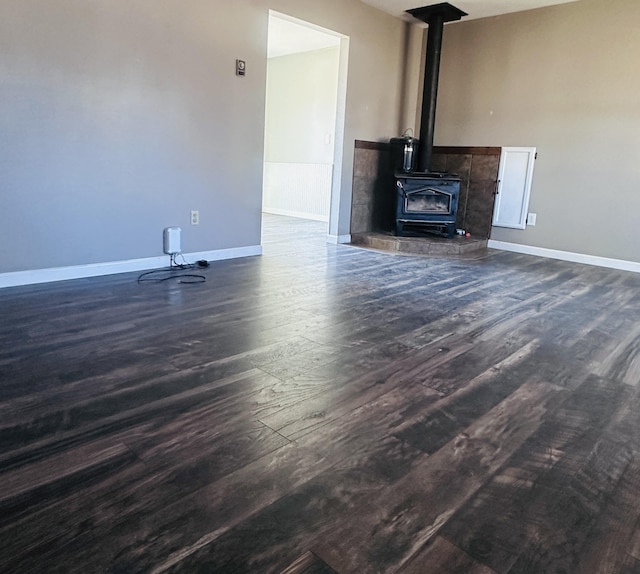 unfurnished living room with dark wood-type flooring, a wood stove, and baseboards