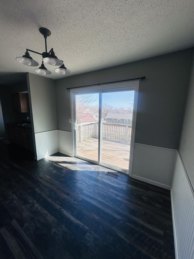 unfurnished room with visible vents, a wainscoted wall, a textured ceiling, and wood finished floors