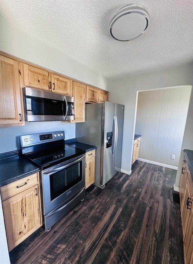 kitchen featuring a textured ceiling, light brown cabinets, appliances with stainless steel finishes, dark wood-style floors, and dark countertops