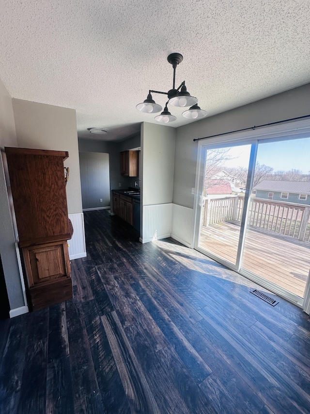 unfurnished living room with a textured ceiling, a wainscoted wall, dark wood-type flooring, a sink, and visible vents