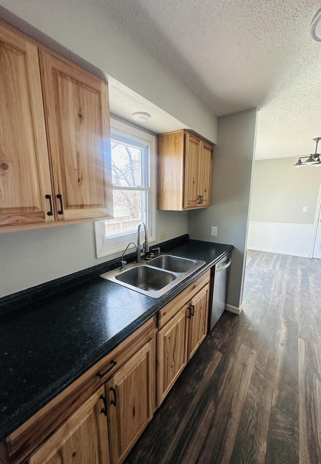 kitchen featuring a textured ceiling, a sink, dishwasher, dark countertops, and dark wood finished floors