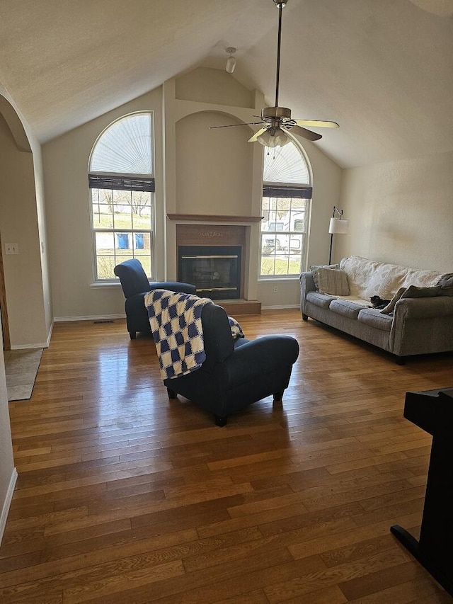 living area featuring arched walkways, a glass covered fireplace, ceiling fan, wood finished floors, and vaulted ceiling