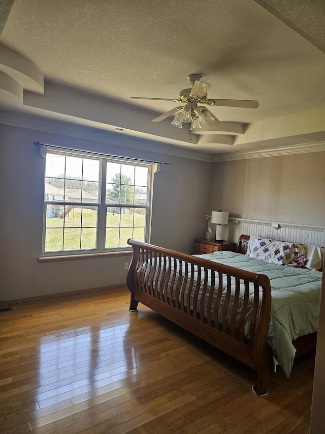 bedroom featuring a textured ceiling, ceiling fan, a tray ceiling, and wood-type flooring