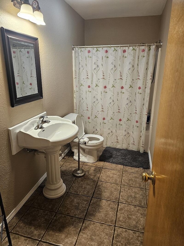 bathroom featuring a textured wall, toilet, shower / bath combo with shower curtain, baseboards, and tile patterned floors