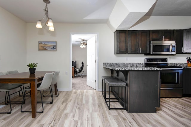 kitchen with appliances with stainless steel finishes, decorative light fixtures, light wood-style floors, and a breakfast bar area