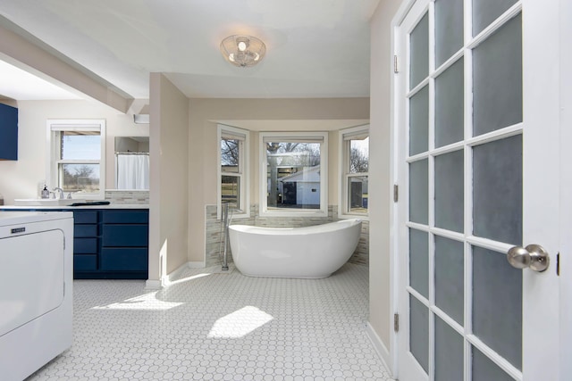 full bath featuring a wealth of natural light, washer / clothes dryer, a freestanding tub, and vanity