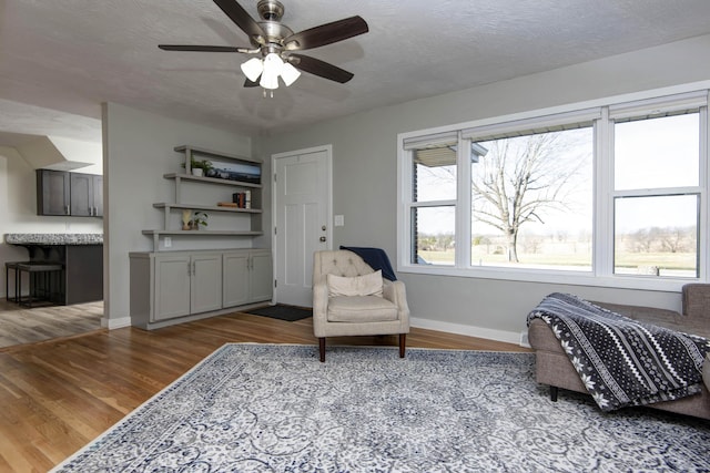 sitting room with ceiling fan, a textured ceiling, baseboards, and wood finished floors