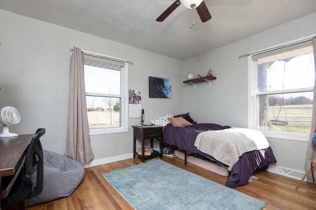 bedroom featuring a ceiling fan, multiple windows, baseboards, and wood finished floors