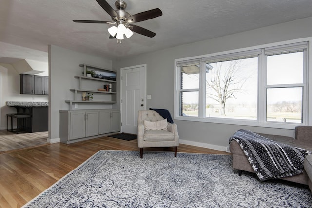 living area with a ceiling fan, a textured ceiling, baseboards, and wood finished floors