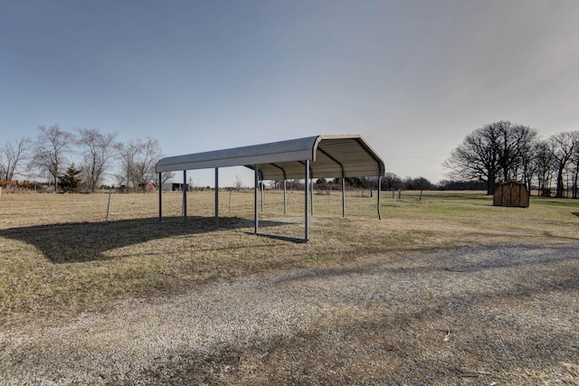 view of yard featuring a detached carport, a rural view, an outdoor structure, and a storage shed