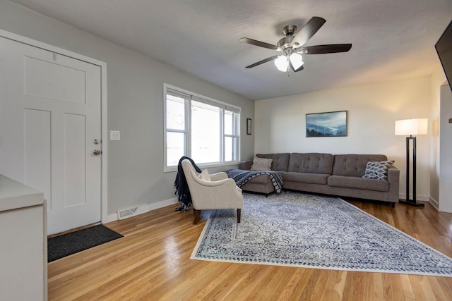 living area featuring a ceiling fan, visible vents, baseboards, and wood finished floors