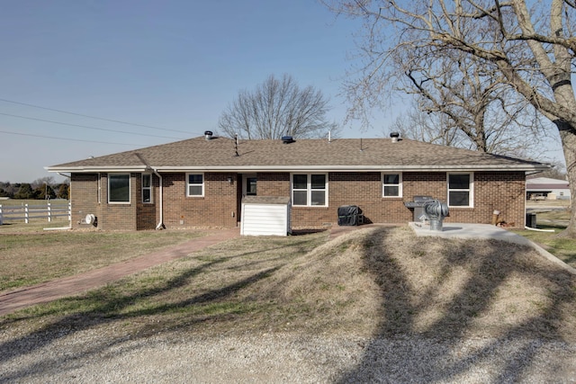 back of property featuring roof with shingles, brick siding, fence, and a lawn