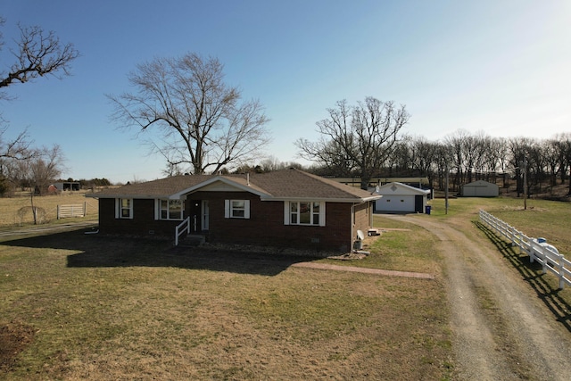 view of front facade with brick siding, an outdoor structure, fence, dirt driveway, and a front lawn