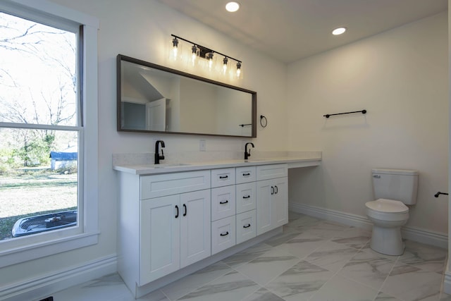 bathroom featuring toilet, marble finish floor, baseboards, and a sink