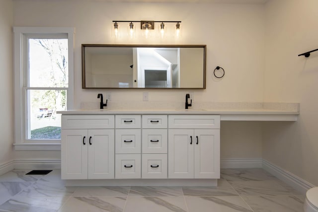 bathroom with double vanity, marble finish floor, baseboards, and a sink