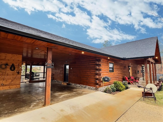 exterior space featuring driveway, an attached carport, log exterior, and roof with shingles