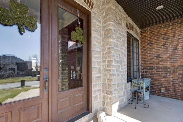 view of exterior entry with a porch, stone siding, and brick siding