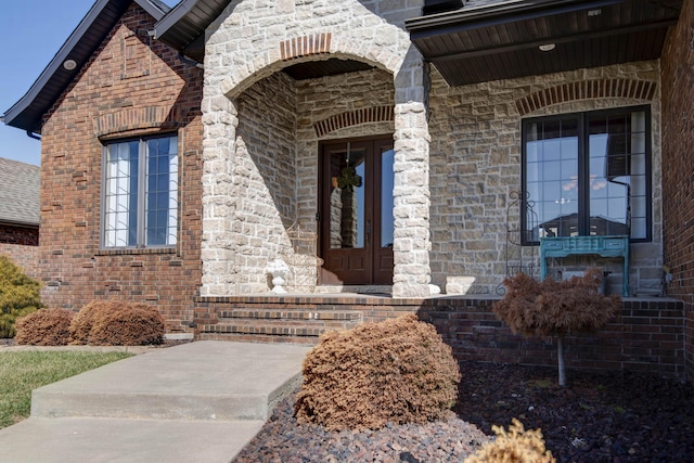 view of exterior entry with stone siding, brick siding, and a shingled roof