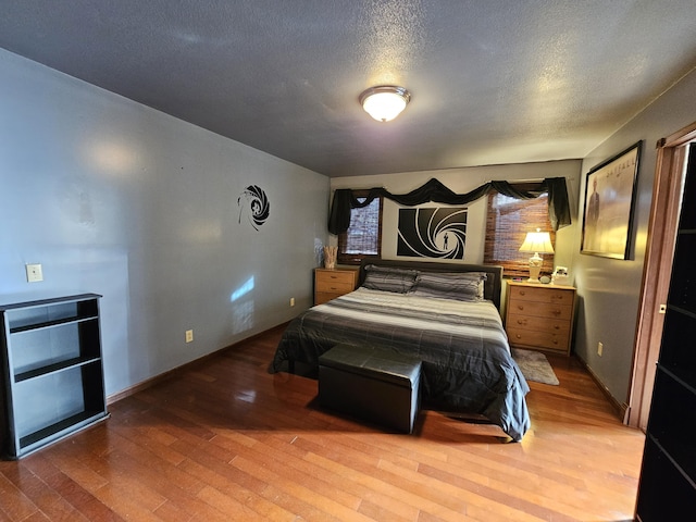 bedroom with a textured ceiling, baseboards, and wood finished floors