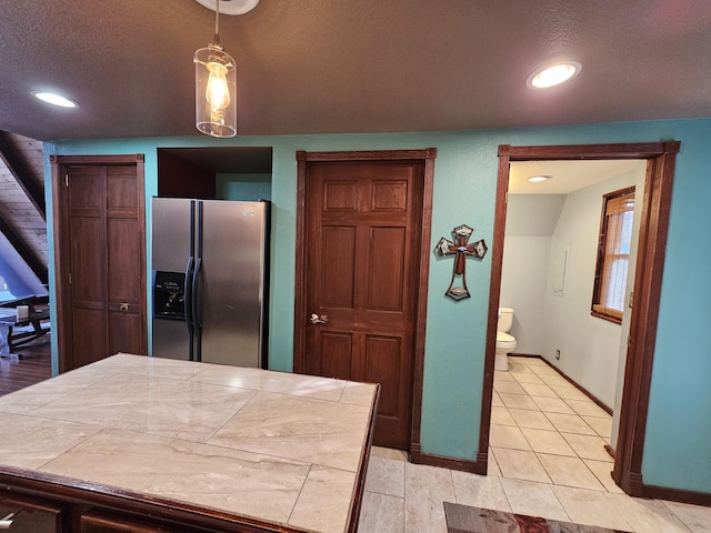 kitchen featuring light tile patterned floors, stainless steel fridge, baseboards, tile countertops, and a textured ceiling