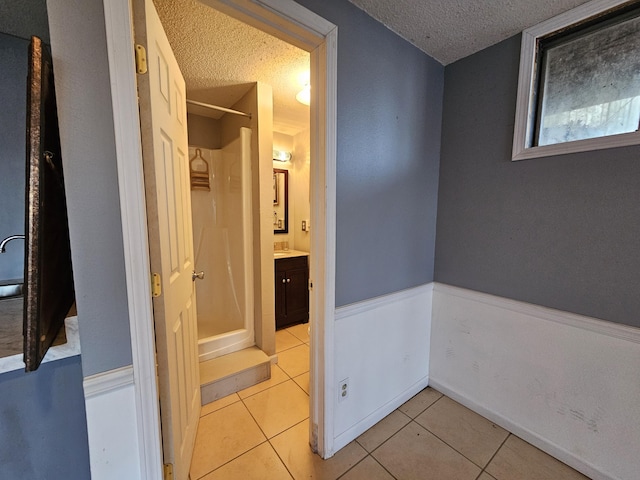 corridor with light tile patterned floors, a textured ceiling, and wainscoting