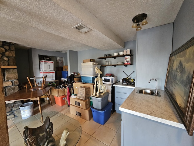 kitchen with light tile patterned floors, light countertops, visible vents, white microwave, and a sink