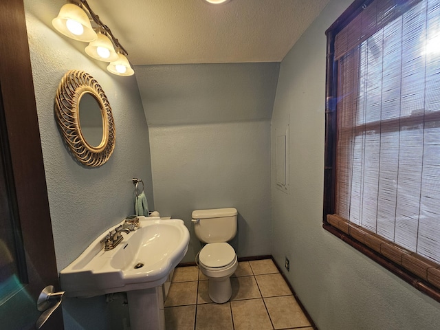 bathroom with baseboards, toilet, tile patterned floors, a textured ceiling, and a sink