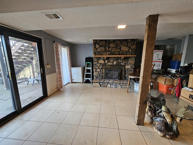 living area featuring light tile patterned floors, a textured ceiling, a fireplace, and visible vents