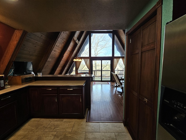 interior space with lofted ceiling with beams, wooden ceiling, dark brown cabinetry, a peninsula, and light countertops