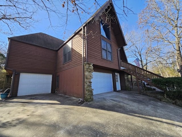 view of side of home featuring roof with shingles, concrete driveway, stairway, an attached garage, and stone siding