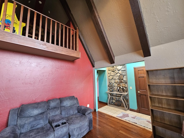 living area with a textured wall, lofted ceiling with beams, and wood finished floors