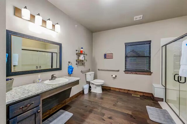 bathroom with toilet, wood finished floors, vanity, baseboards, and a stall shower