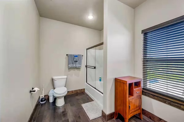 full bath with baseboards, toilet, shower / bath combination with glass door, wood finished floors, and a wealth of natural light