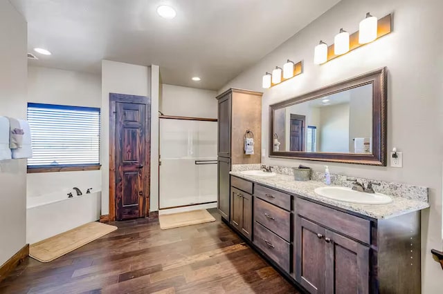 bathroom with a tub to relax in, double vanity, wood finished floors, a sink, and recessed lighting